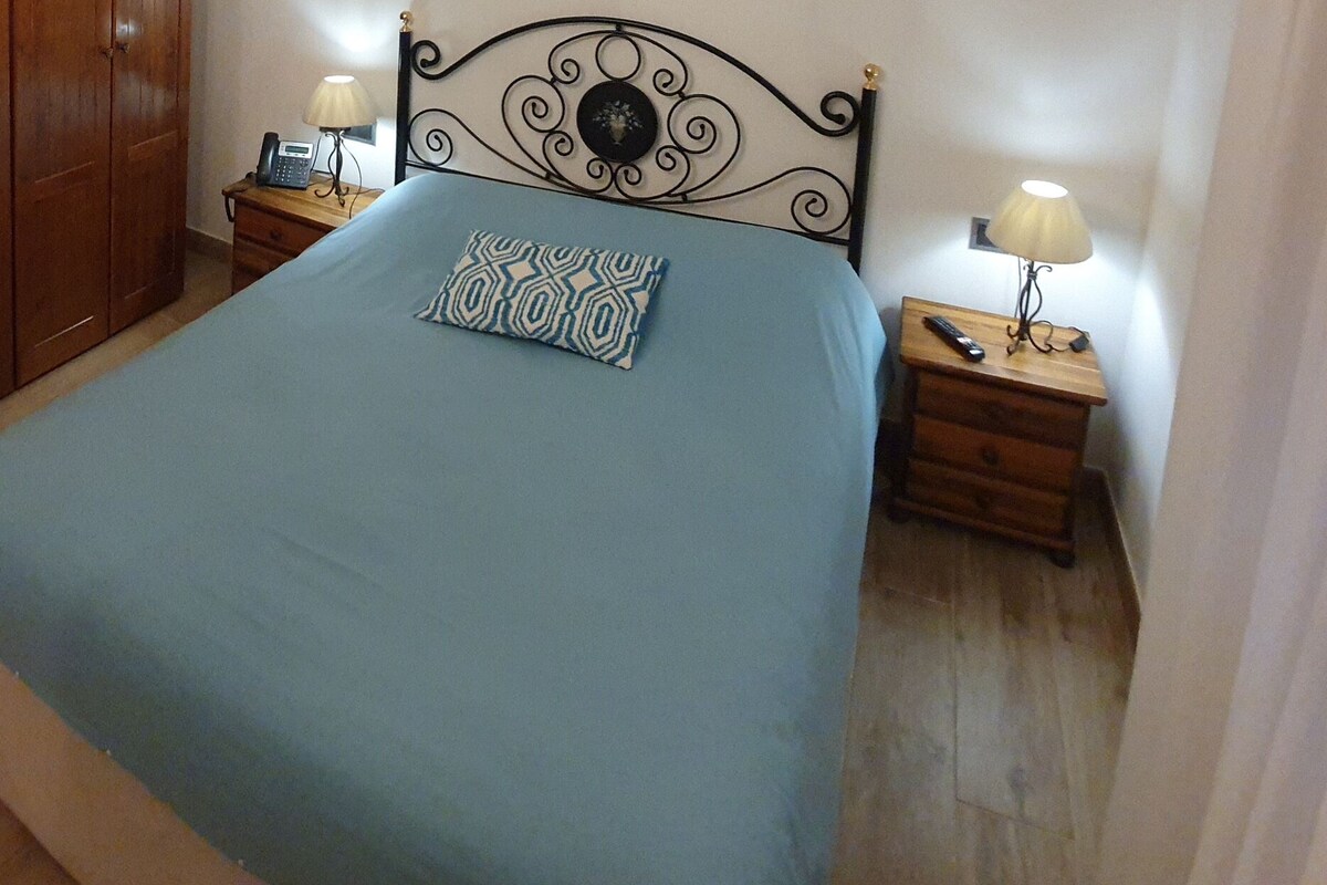 Une chambre à coucher comprenant un lit, une armoire en bois, des tables de chevet avec des lampes et une petite table de nuit.
