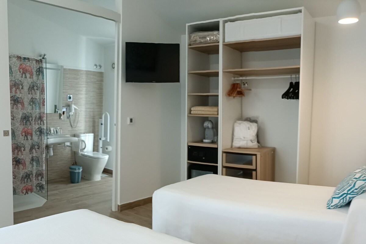 Une chambre à coucher comprenant un lit, une armoire, un téléviseur et une salle de bain avec douche et toilettes.