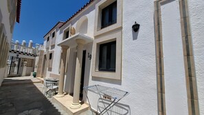 A building with a white facade, columns, and a balcony with a metal chair and table.