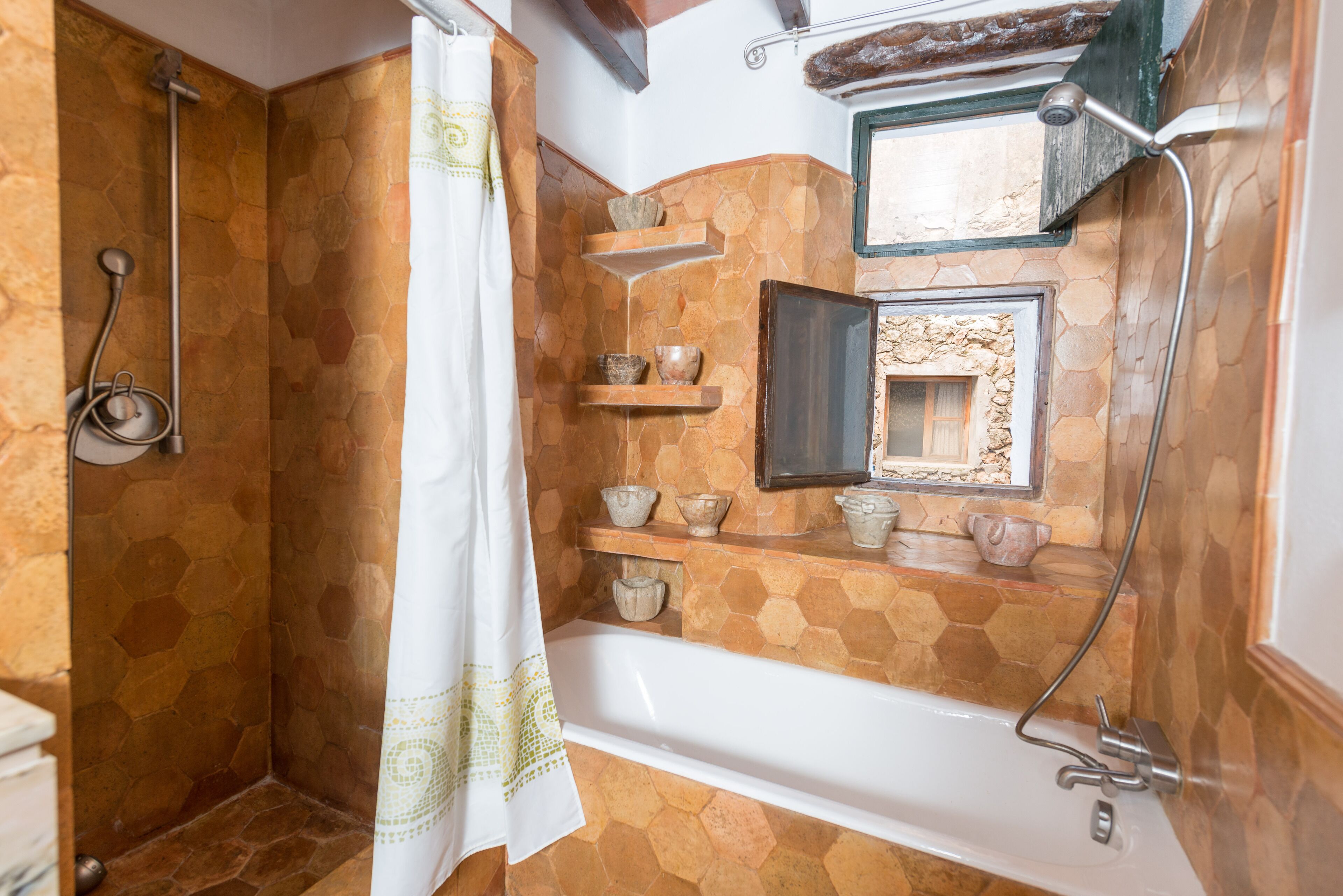 A bathroom with a hexagonal tile pattern, a bathtub, a shower, and shelves with decorative items.