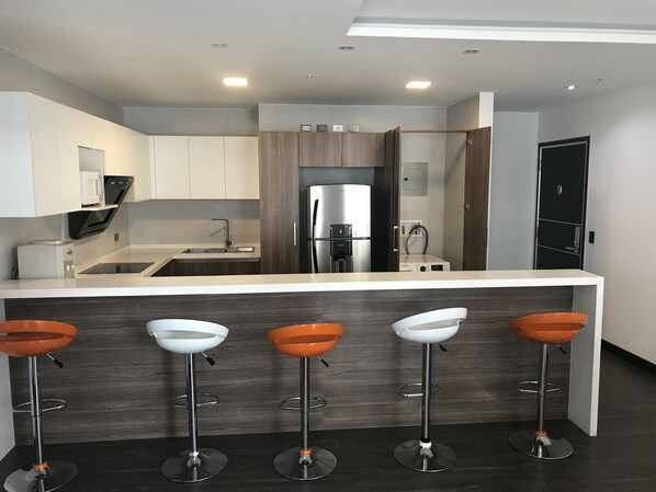 A modern kitchen with a central island, four bar stools, a refrigerator, and a microwave. - EXCLUSIVE DEPARTMENT (Quito)