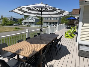 Eine Holzterrasse mit Tisch und Stühlen, einem gestreiften Sonnenschirm und einem weißen Zaun.