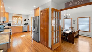 A spacious kitchen with wooden cabinets, a stainless steel refrigerator, and a dining area with a wooden table and chairs. - York Beach Getaway (Razzle Dazzle House) (York)