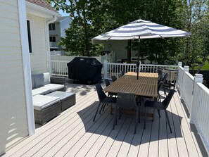Eine Holzterrasse mit Tisch, Stühlen, einem Grill und einem überdachten Grillbereich.