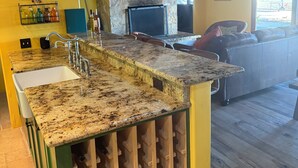 A kitchen with a granite countertop, a built-in wine rack, and a stone fireplace. - Vineyard Home for the Art Lover (Santa Ynez)