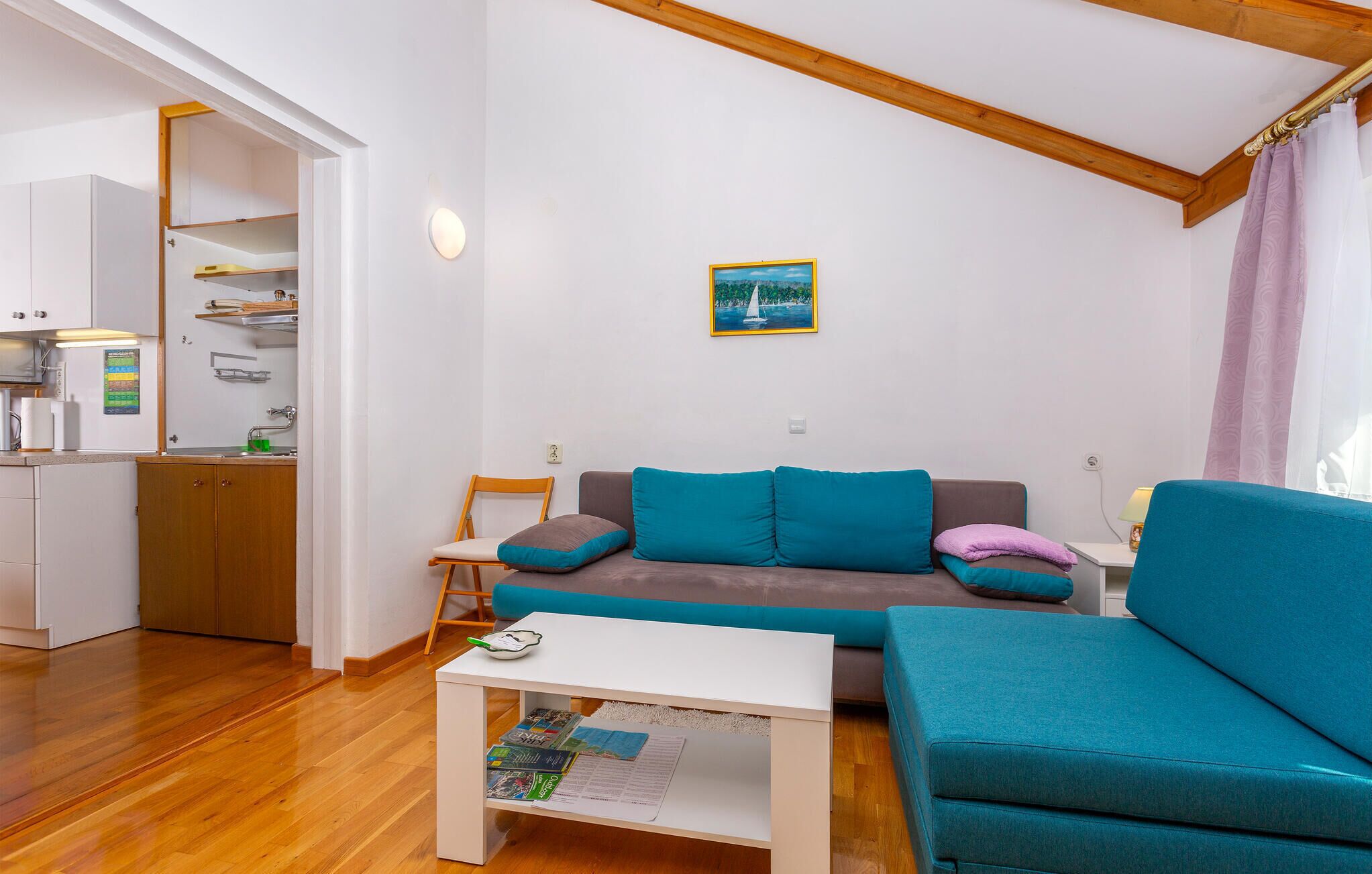 Ein modernes Wohnzimmer mit einer Couch, einem Couchtisch und einem durchgehenden Gang sichtbarem Küchenbereich.