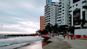 Una playa con una hilera de edificios altos, palmeras y un mar tranquilo.