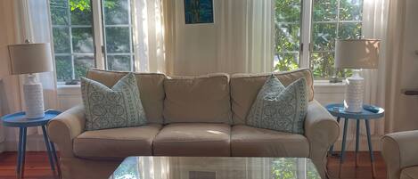 Una sala de estar con una mesa de centro de vidrio, sofá color crema y dos mesitas de noche con lámparas.