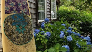 A surfboard with a floral design leaning against a wooden house with a window. - TRANQUILITY IN NANTUCKET (Nantucket)