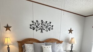 A neatly arranged bedroom with a large bed, two bedside tables with lamps, decorative wall art, and a wooden bench. - Peaceful Hill Country Retreat • Private Hot Tub • 3½ Acres • Near Downtown (Wimberley)