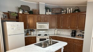 A modern kitchen with wooden cabinets, a white refrigerator, a built-in oven, a microwave, and a marble countertop. - Peaceful Hill Country Retreat • Private Hot Tub • 3½ Acres • Near Downtown (Wimberley)