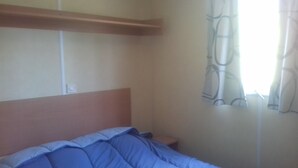 Une chambre à coucher avec un lit, une table de chevet, une prise électrique et une fenêtre avec des rideaux.