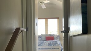 Un corridoio che porta a una camera da letto con un letto, una ventola a soffitto e una finestra con tende.