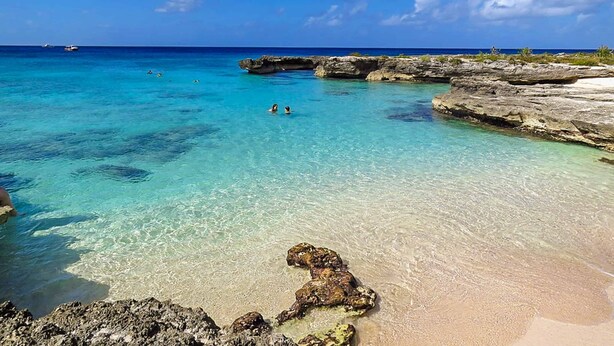 Un mare turchese cristallino con formazioni rocciose e una spiaggia sabbiosa.