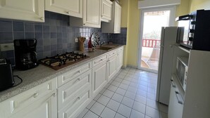 Una cocina con armarios blancos, estufa a gas, cafetera y refrigerador.