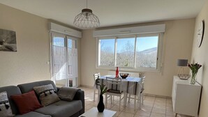 Una sala de estar con un sofá gris, una mesita y un comedor con una mesa y sillas blancas.