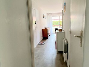 Un couloir étroit avec un radiateur, un meuble en bois et une table sur laquelle se trouve un vase.