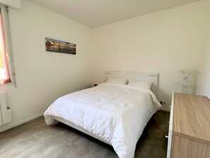 A bedroom with a bed, a nightstand, a chair, a painting on the wall, and a window.
