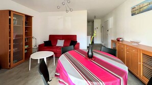 A compact living space with a red sofa, a dining table with a striped tablecloth, a wooden cabinet, and a bookshelf.