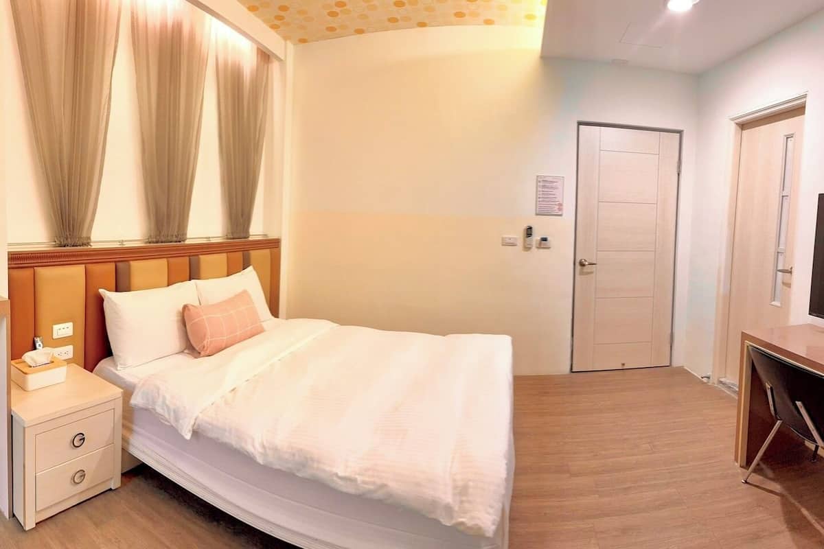 A hotel room with a bed, bedside table, TV, and a desk.