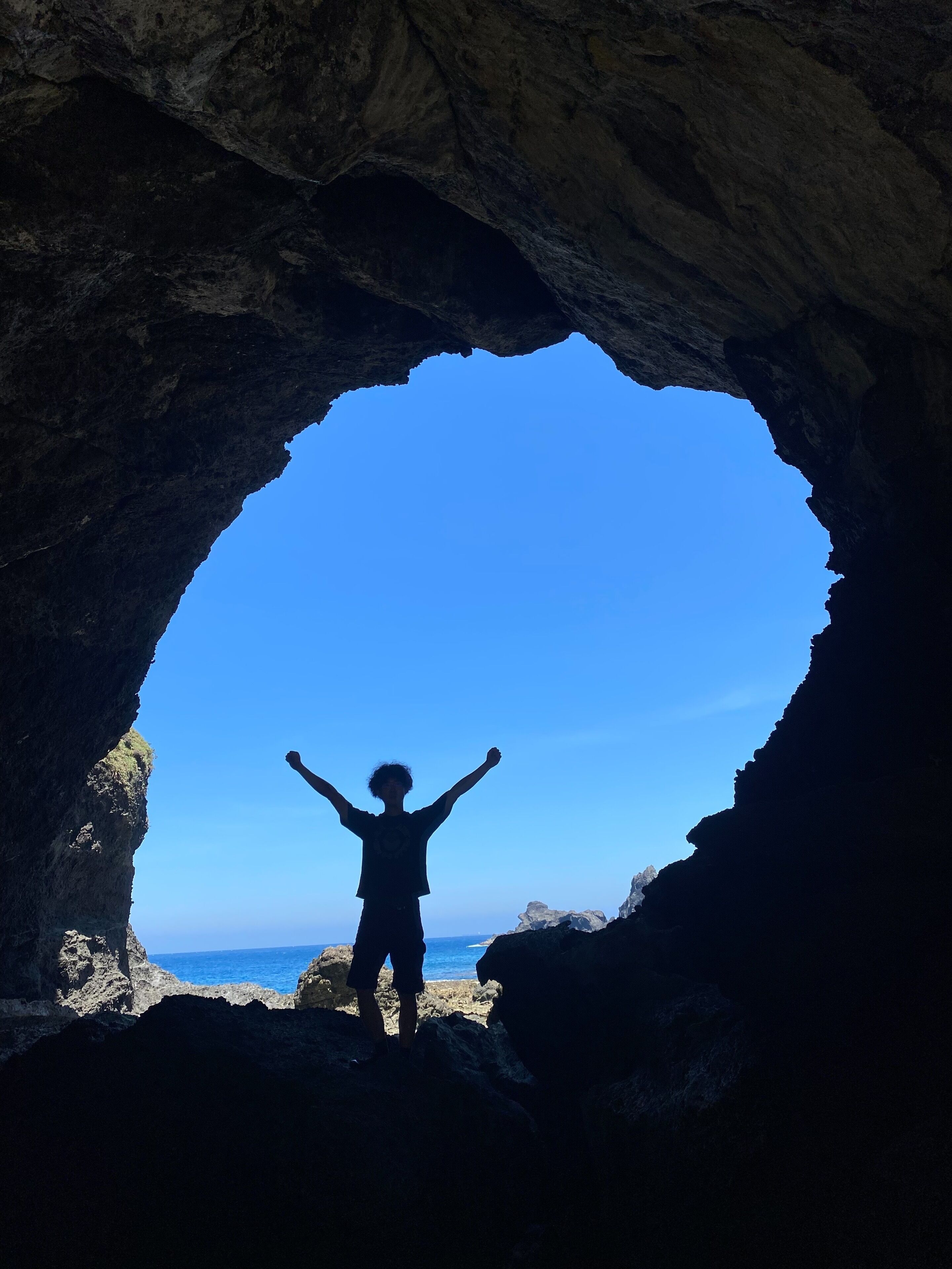 A person standing in a cave with a clear view of the ocean.