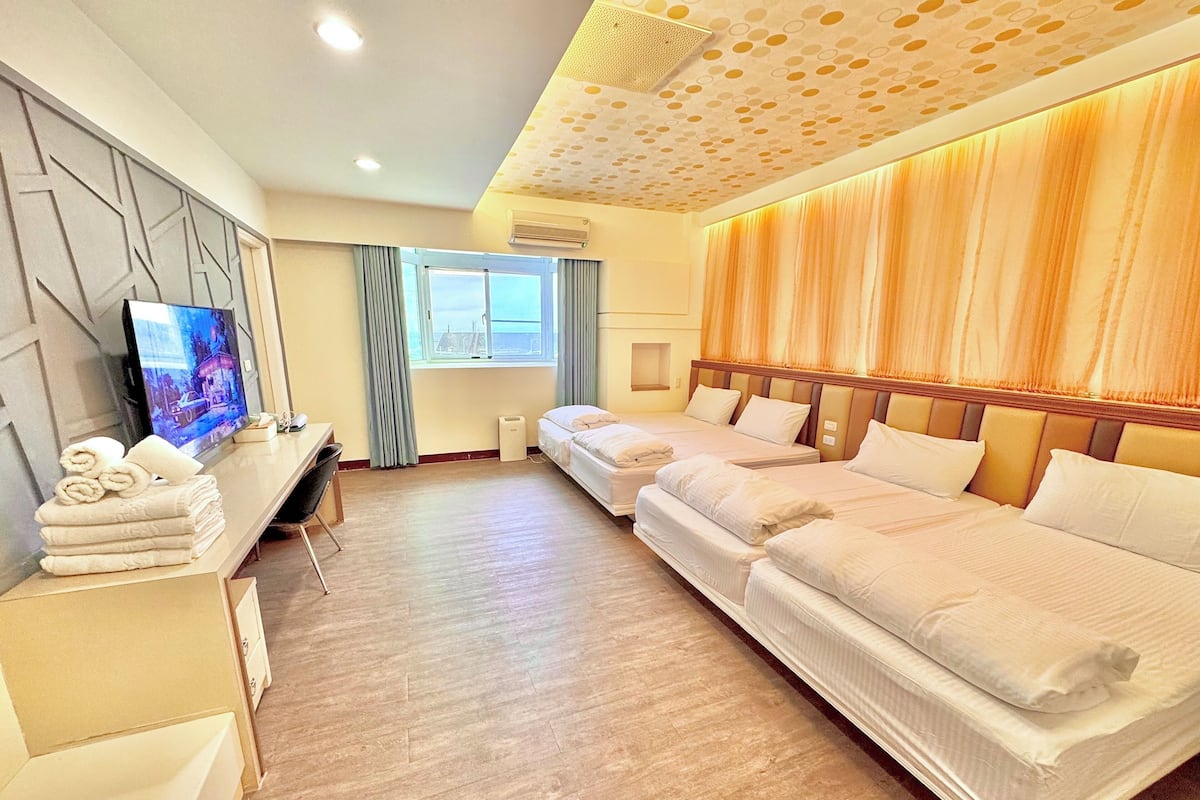 A hotel room with a TV, two beds, a desk, and a window with curtains.