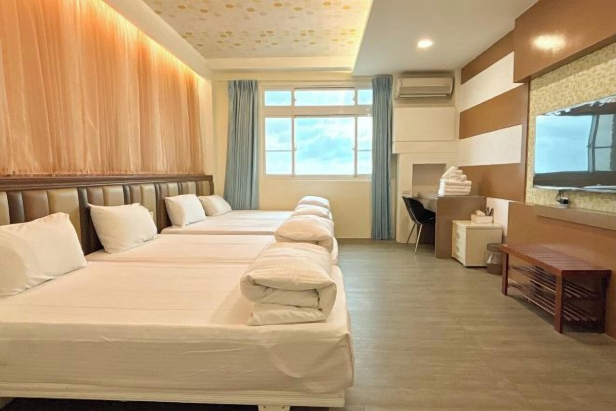 A hotel room with two beds, a desk, a chair, a small table, and a window with curtains.
