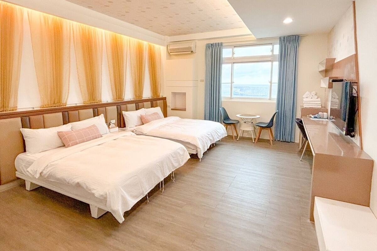 A hotel room with two beds, a small table with chairs, a TV, and a window with curtains.
