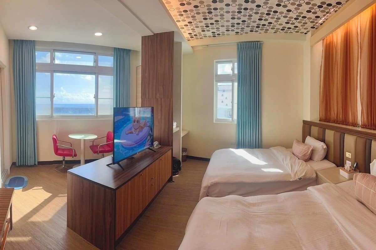 A hotel room with a large bed, a TV, a desk, and a view of the sea.