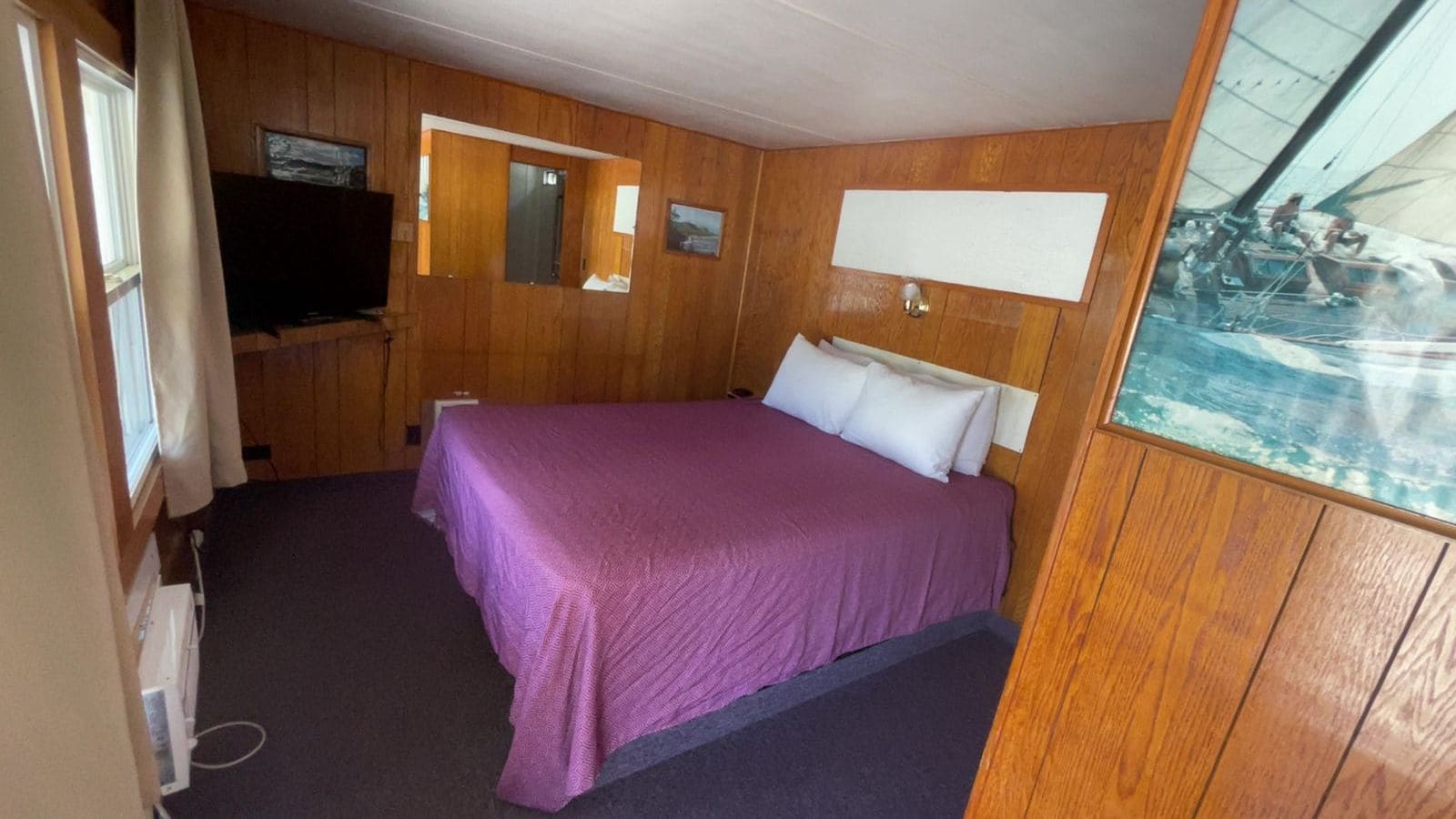 A room with a bed, wooden walls, a television, and a window.