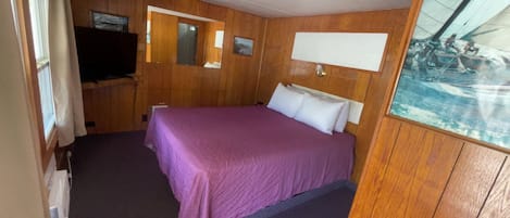 A room with a bed, wooden walls, a television, and a window.