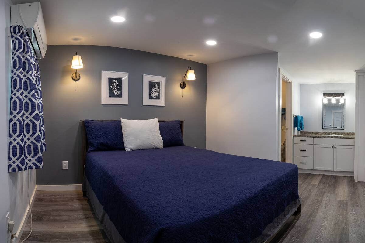 A bedroom with a large bed, two wall-mounted light fixtures, and a bathroom visible through an open door.
