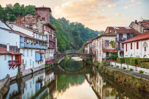 Un canal flanqueado por edificios, un puente y abundante vegetación al fondo.