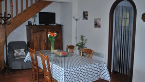 A dining area with a table set for four, surrounded by wooden chairs. A television is mounted on a wooden cabinet above the table. - Charming Small Cottage in Soule (MENDITTE)
