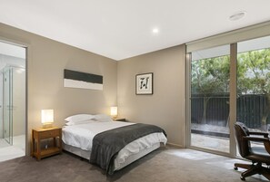 A bedroom with a bed, bedside lamps, a framed picture, and a view of the outdoors.