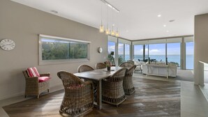 A modern dining area with wicker furniture, a large window, and a view of the sea. - Grossard Point The Lighthouse Ventnor (Ventnor)