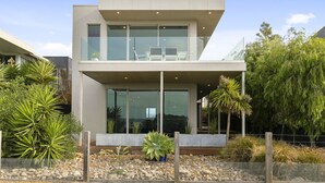 A modern two-story house with a balcony, large windows, and a garden with various plants. - Grossard Point The Lighthouse Ventnor (Ventnor)