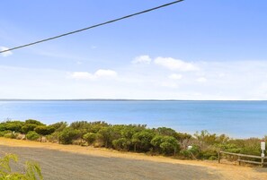 A coastal road with a view of the sea, surrounded by greenery and a clear sky.
