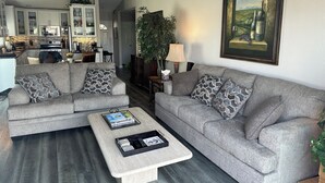A modern living room with two grey sofas, a coffee table, and a painting of wine bottles.
