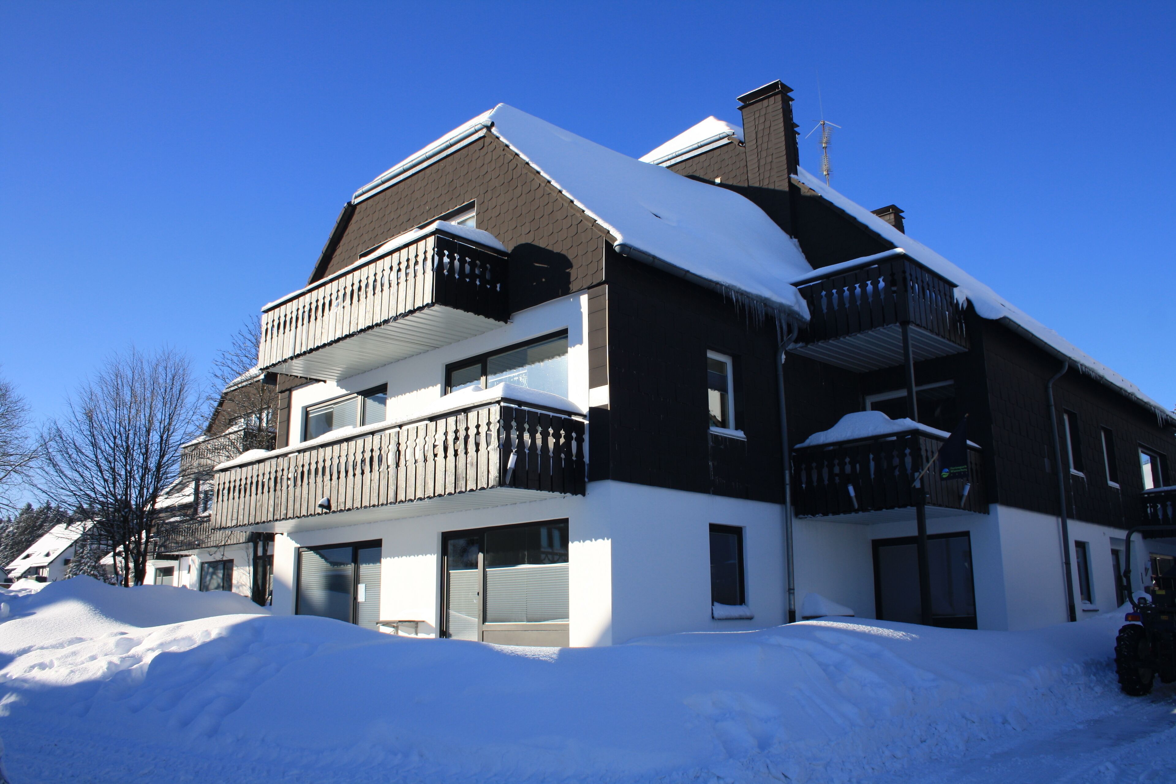 A two-story building with a balcony on the second floor, a garage, and a snow-covered roof.