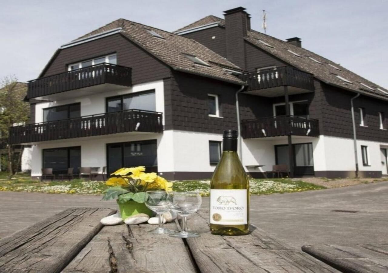 A modern two-story building with balconies, a bottle of wine, and a vase with flowers on a wooden table.