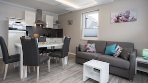 A modern living room with a grey sofa, black chairs, a small white table, and a kitchen area with white cabinets and a black countertop. - Ferienpark Winterberg (Winterberg)