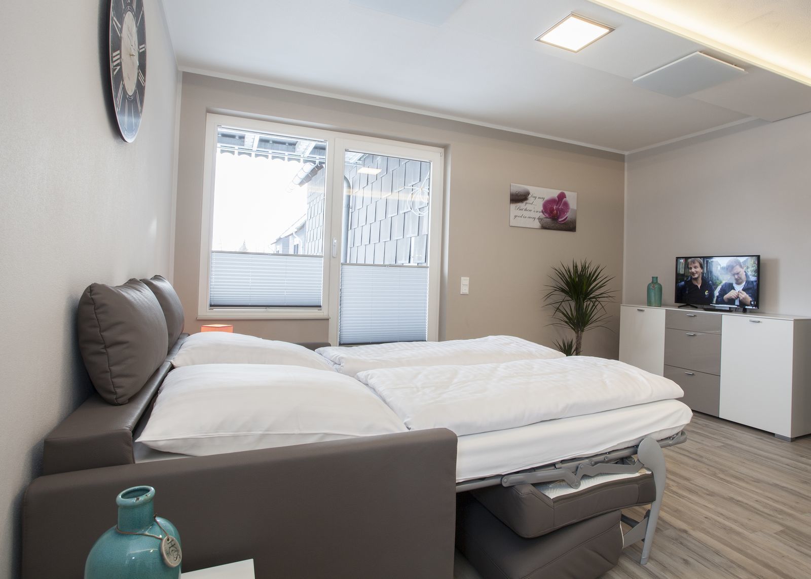 Une chambre moderne avec un lit, une table de chevet, une lampe et un téléviseur posé sur une commode.