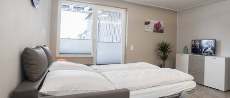 Une chambre moderne avec un lit, une table de chevet, une lampe et un téléviseur posé sur une commode.