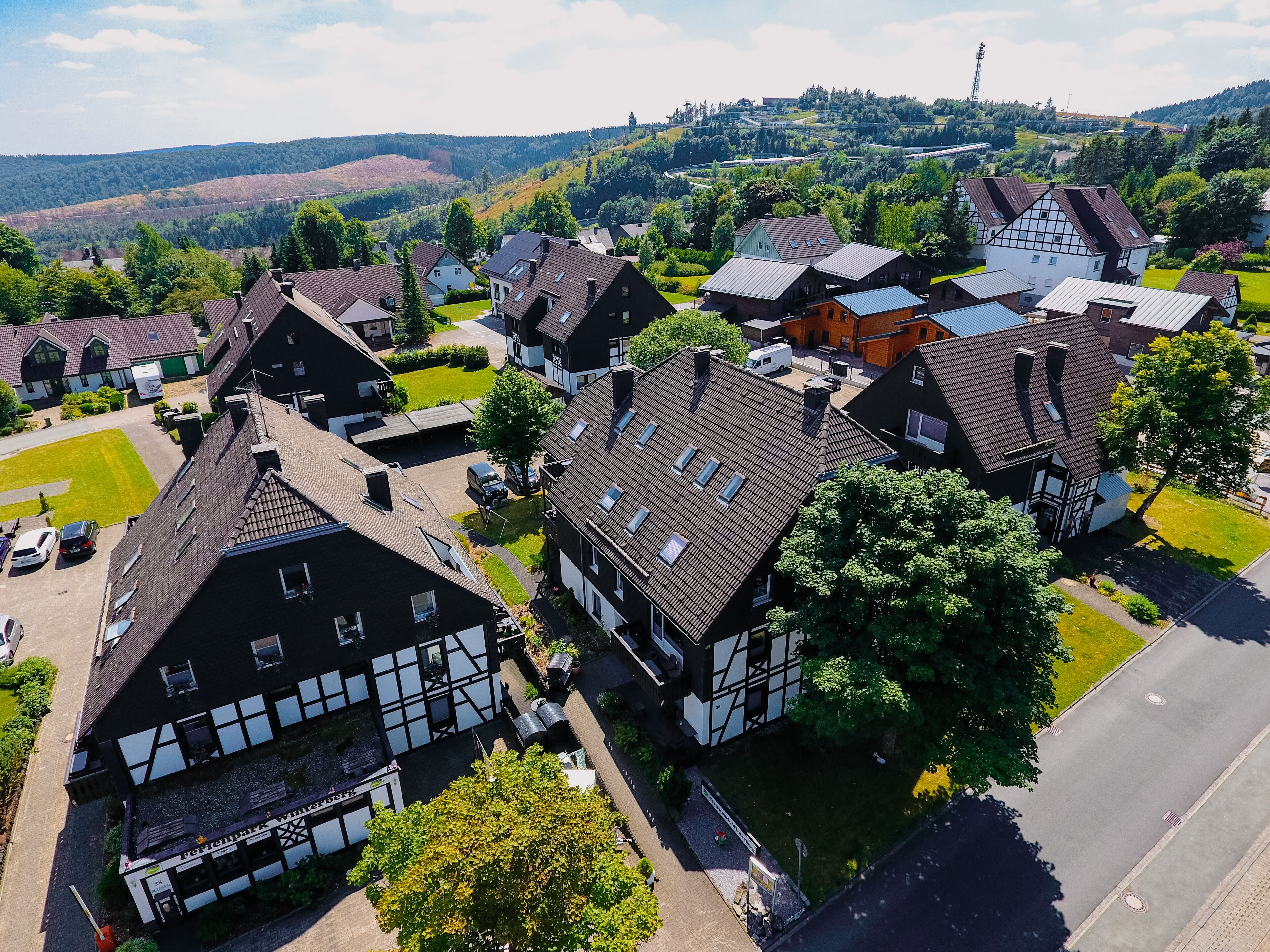A traditional European village with timber-framed houses, a central pub, and a road leading to a hilltop.