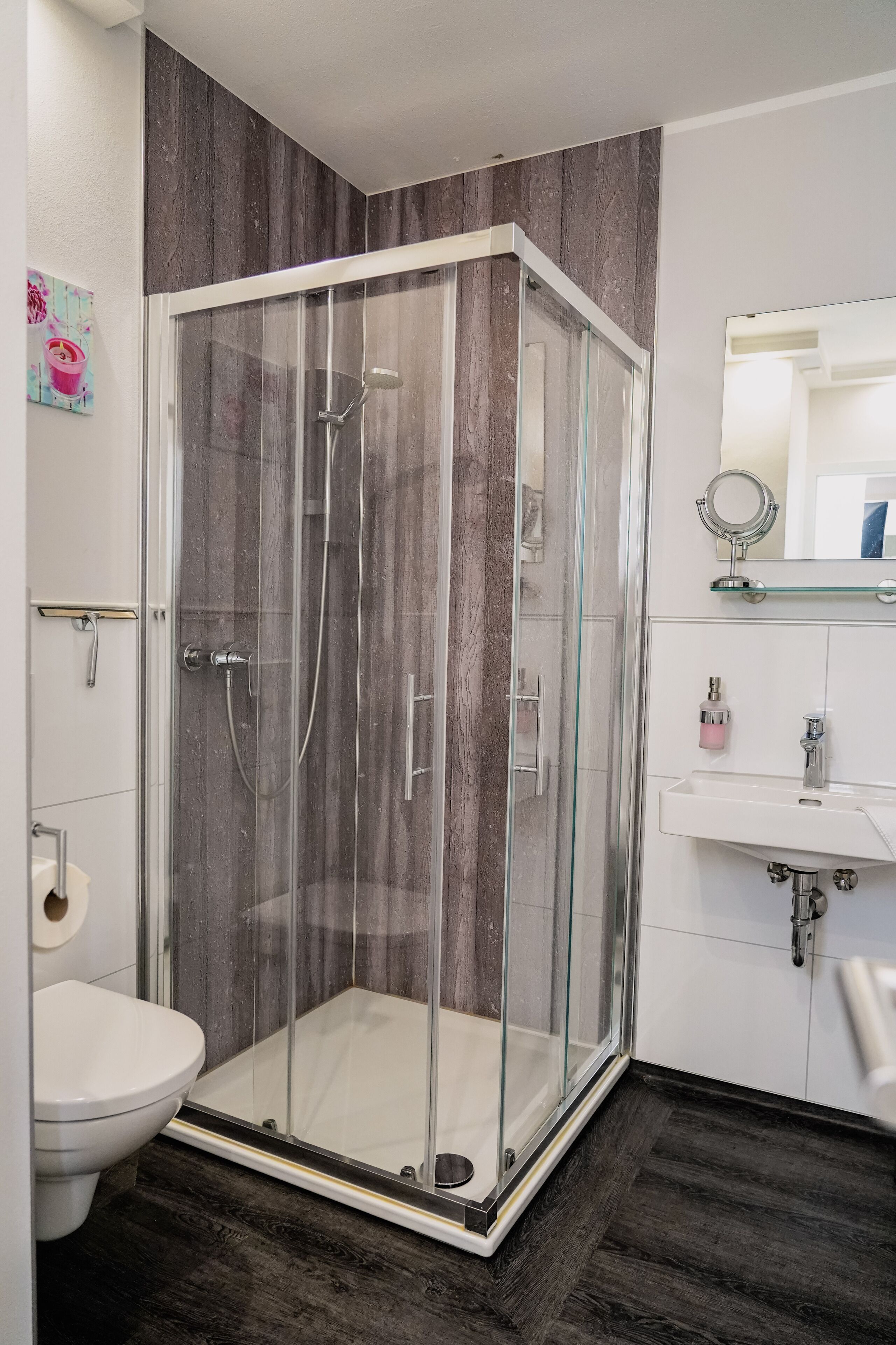 A modern bathroom with a glass-enclosed shower, a white toilet, and a vanity with a mirror and sink.