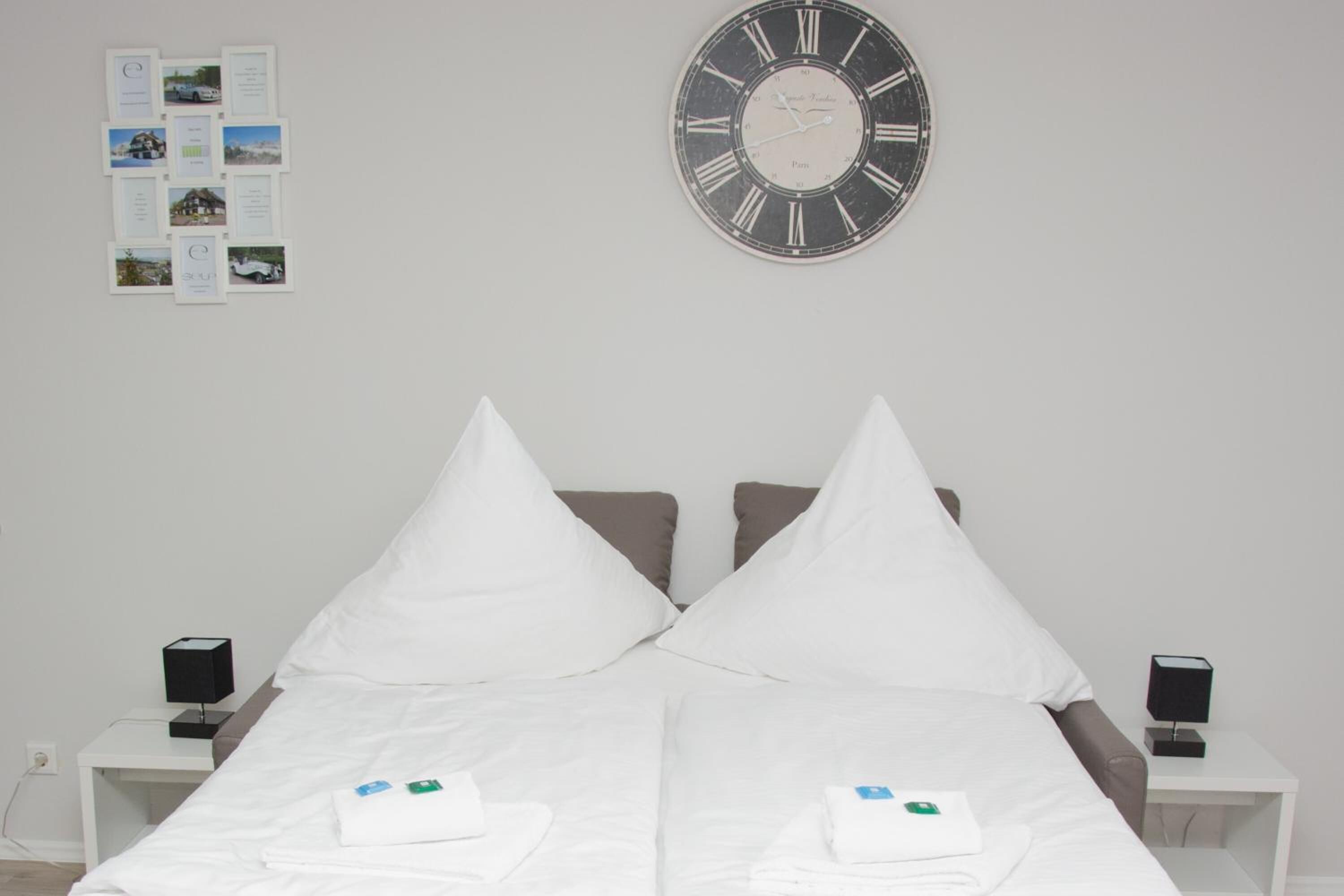 A hotel room with a bed, two nightstands, a clock, and a bulletin board with photos.
