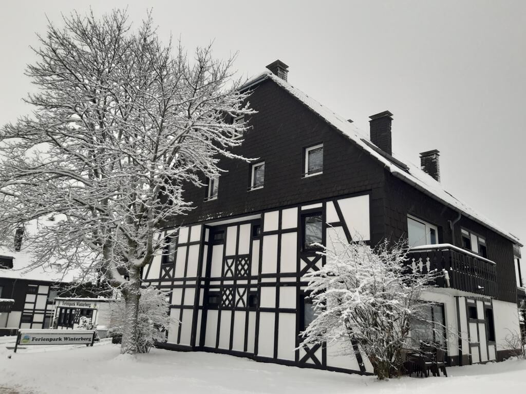 A traditional half-timbered house with a steeply pitched roof, surrounded by snow-covered trees and a sign for 'Felsenpark Winterberg'.