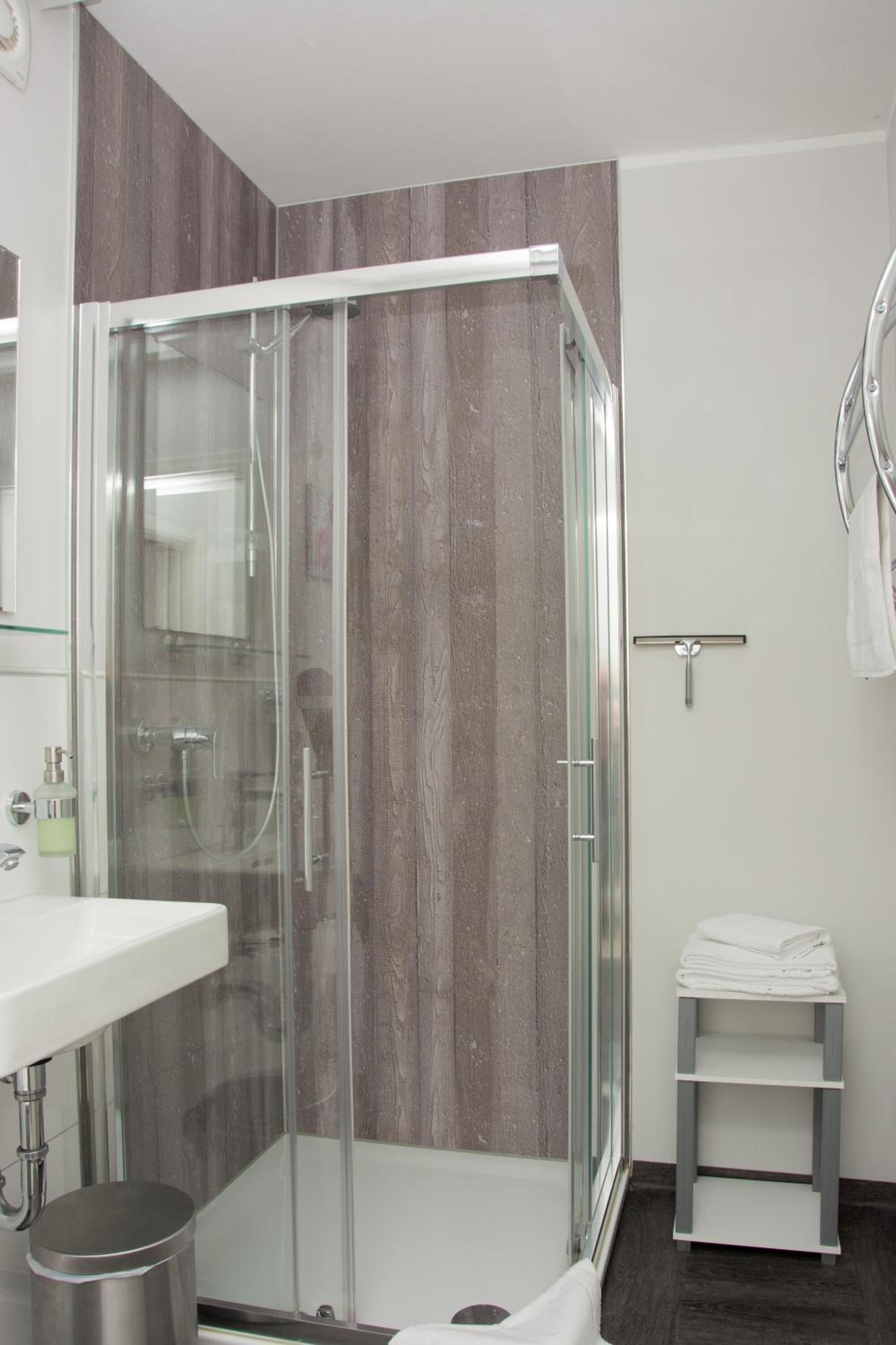 A modern bathroom with a glass-enclosed shower, a white sink, and a towel rack.