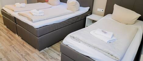Two twin beds with white linens and pillows, a wooden floor, and a small bedside table with a lamp.